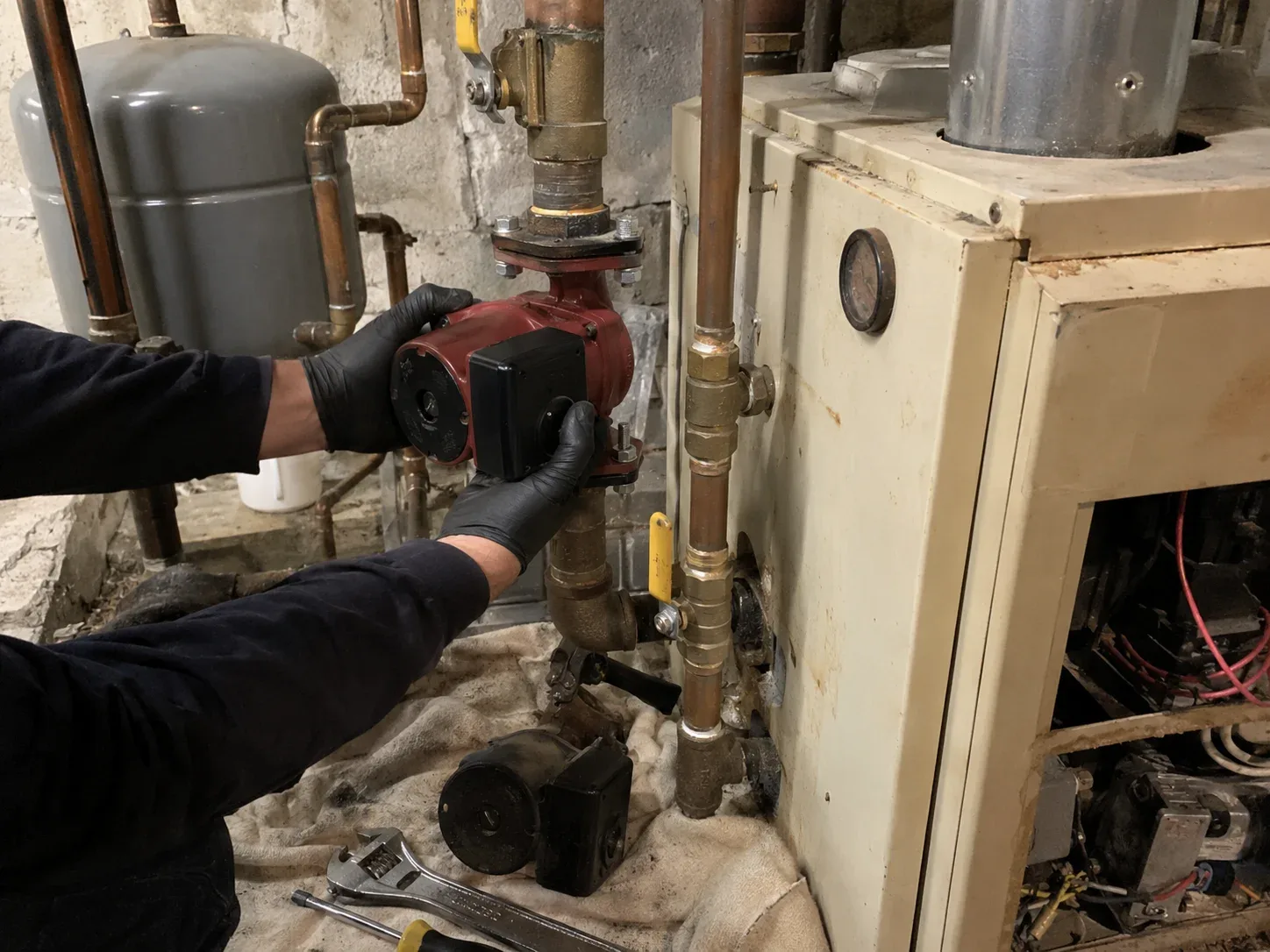 Technician inspecting internal components of an older wall-mounted boiler